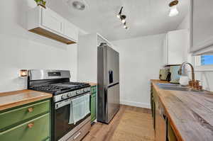 Kitchen featuring appliances with stainless steel finishes, butcher block countertops, sink, and white cabinetry