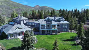 Rear view of house featuring a chimney, a balcony, a lawn, stone siding, and a mountain view
