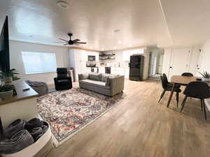 Living room with ceiling fan, a textured ceiling, and light hardwood / wood-style floors