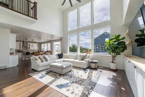 Living room with a high ceiling, ceiling fan, and dark wood-type flooring