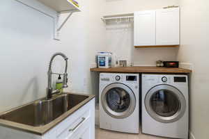 Laundry room with light tile patterned floors, cabinets, sink, and washer and dryer