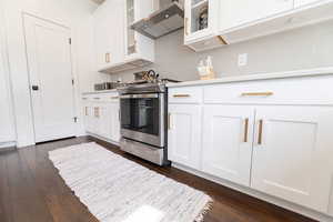 Kitchen with wall chimney range hood, white cabinetry, stainless steel range oven, dark hardwood / wood-style flooring, and decorative backsplash