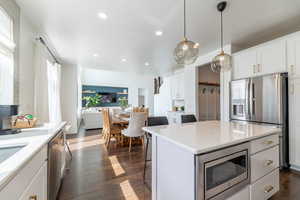 Kitchen with dark hardwood / wood-style floors, white cabinets, a kitchen island, stainless steel appliances, and decorative light fixtures