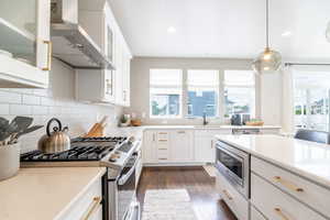 Kitchen with white cabinetry, stainless steel appliances, dark hardwood / wood-style floors, wall chimney range hood, and sink