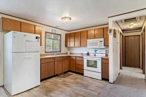 Kitchen featuring a textured ceiling, sink, light hardwood / wood-style flooring, white appliances, and ornamental molding