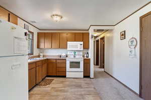 Kitchen featuring light hardwood / wood-style floors, white appliances, a textured ceiling, crown molding, and sink