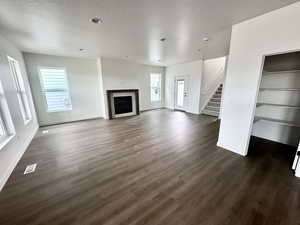 Unfurnished living room with a textured ceiling, a healthy amount of sunlight, and dark wood-type flooring