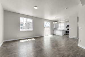 Unfurnished living room featuring a notable chandelier, a textured ceiling, dark wood-type flooring, and sink