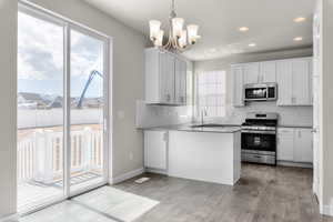 Kitchen with pendant lighting, stainless steel appliances, white cabinets, and light hardwood / wood-style floors