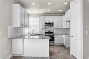 Kitchen featuring wood-type flooring, sink, white cabinets, kitchen peninsula, and stainless steel appliances