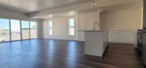 Kitchen with dark hardwood / wood-style floors, sink, white cabinets, hanging light fixtures, and a center island with sink