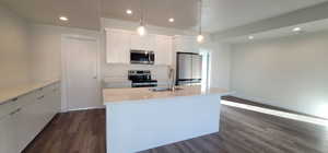 Kitchen with hanging light fixtures, a kitchen island with sink, white cabinetry, appliances with stainless steel finishes, and dark hardwood / wood-style flooring