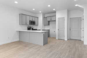 Kitchen featuring a breakfast bar, light hardwood / wood-style floors, kitchen peninsula, gray cabinetry, and appliances with stainless steel finishes