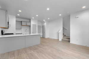 Kitchen with gray cabinetry, kitchen peninsula, light wood-type flooring, stove, and sink