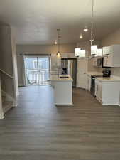 Kitchen with appliances with stainless steel finishes, a kitchen island with sink, white cabinets, and decorative light fixtures