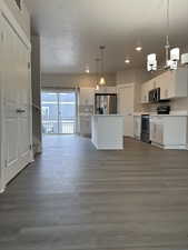 Kitchen featuring appliances with stainless steel finishes, decorative light fixtures, wood-type flooring, white cabinets, and a center island