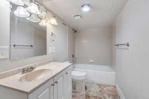 Full bathroom featuring vanity, tiled shower / bath combo, toilet, and a textured ceiling