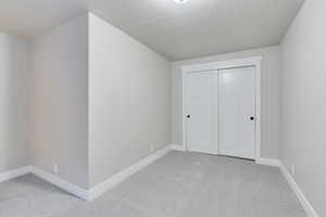 Unfurnished bedroom featuring a closet, light colored carpet, and a textured ceiling