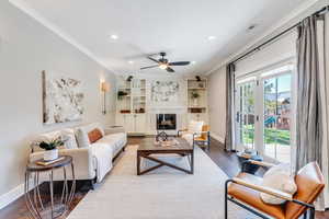 Living room with a fireplace, ceiling fan, built in features, hardwood / wood-style flooring, and ornamental molding