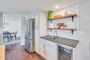 Kitchen featuring dark wood-type flooring, stainless steel refrigerator, backsplash, beverage cooler, and sink