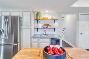 Kitchen with stainless steel fridge with ice dispenser, sink, beverage cooler, white cabinets, and backsplash