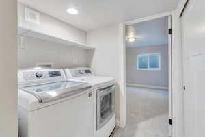 Laundry area featuring light carpet and washer and clothes dryer