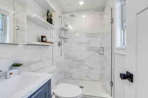 Bathroom featuring tile walls, backsplash, vanity, walk in shower, and toilet