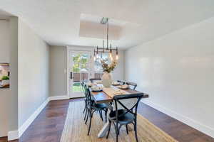 Dining space with a notable chandelier, a textured ceiling, a tray ceiling, and dark wood-type flooring