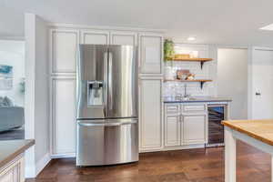 Kitchen featuring stainless steel fridge with ice dispenser, beverage cooler, white cabinets, decorative backsplash, and dark hardwood / wood-style flooring