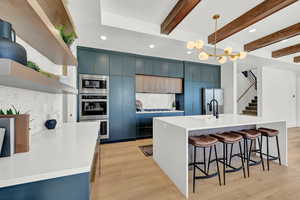 Kitchen featuring beam ceiling, light wood-type flooring, blue cabinets, and appliances with stainless steel finishes