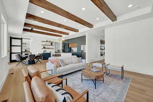 Living room with light wood-type flooring, a barn door, an inviting chandelier, and beamed ceiling