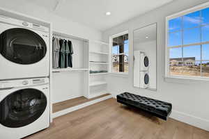 Laundry area with light hardwood / wood-style flooring and stacked washing maching and dryer