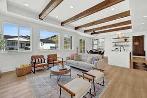 Living room with a healthy amount of sunlight, light hardwood / wood-style floors, a chandelier, and beamed ceiling