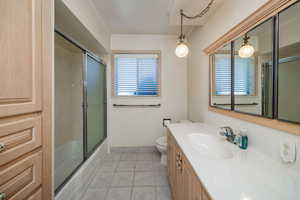 Full bathroom with enclosed tub / shower combo, vanity, tile patterned flooring, crown molding, and toilet