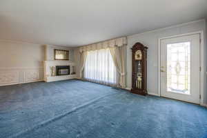 Unfurnished living room featuring carpet floors, a healthy amount of sunlight, a fireplace, and crown molding