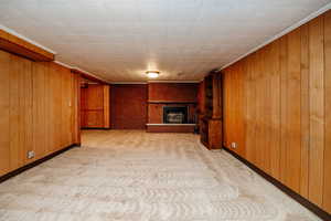 Unfurnished living room featuring crown molding, wood walls, light colored carpet, and a brick fireplace