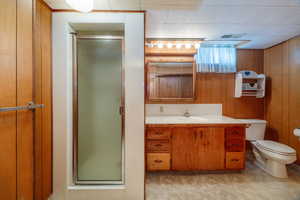 Bathroom featuring wood walls, a shower with door, toilet, and vanity