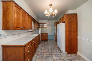 Kitchen featuring backsplash, white appliances, pendant lighting, crown molding, and a chandelier