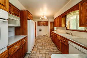 Kitchen with hanging light fixtures, sink, white appliances, a chandelier, and decorative backsplash