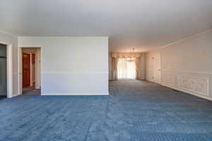 Carpeted spare room featuring crown molding and a notable chandelier