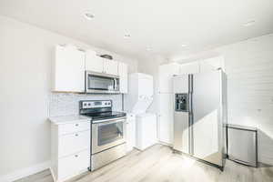 Kitchen with stacked washer and clothes dryer, light hardwood / wood-style flooring, white cabinets, stainless steel appliances, and backsplash