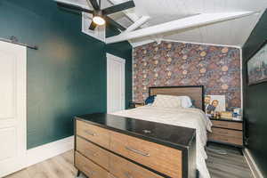 Bedroom featuring a barn door, vaulted ceiling with beams, ceiling fan, and light hardwood / wood-style flooring