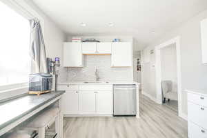 Kitchen with sink, white cabinets, backsplash, stainless steel dishwasher, and light hardwood / wood-style floors