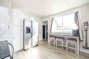 Kitchen featuring a breakfast bar, white electric stove, white cabinets, stainless steel refrigerator with ice dispenser, and light wood-type flooring