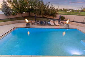 Pool at dusk featuring pool water feature, a patio, and a fire pit