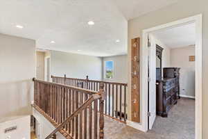 Corridor featuring a textured ceiling and light carpet