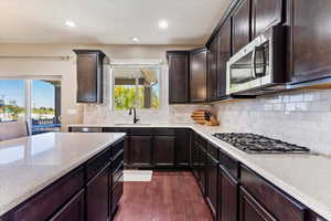 Kitchen with appliances with stainless steel finishes, dark wood-type flooring, backsplash, dark brown cabinets, and sink