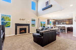 Living room with a towering ceiling, dark hardwood / wood-style flooring, a chandelier, and a brick fireplace