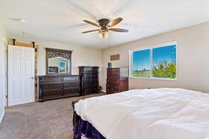 Bedroom with a textured ceiling, ceiling fan, light colored carpet, and a barn door