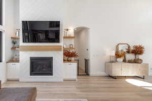 Living room with a towering ceiling, light hardwood / wood-style flooring, and a large fireplace